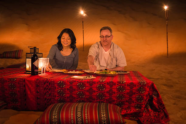 Dubai iStockalypse.  A mature, multi-ethnic couple enjoy a private, traditional Arab, Middle Eastern dinner while on a luxury tour of the red desert between Dubai to Sharjah, United Arab Emirates.  The desert camp is lit by candles, lanterns, and torches amid the sand dunes and is decorated with traditionally patterned pillows and tablecloth.